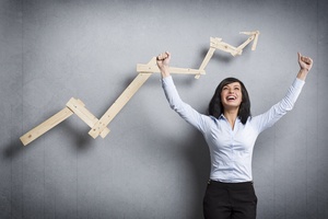 Concept: Success in business or career. Enthusiastic businesswoman with raised arms cheering in front of positive business graph, isolated on grey background.