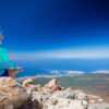 Young woman doing yoga meditation outside natural beautiful inspirational environment fitness and exercising motivation and inspiration in sunny mountains over blue sky and ocean sea.